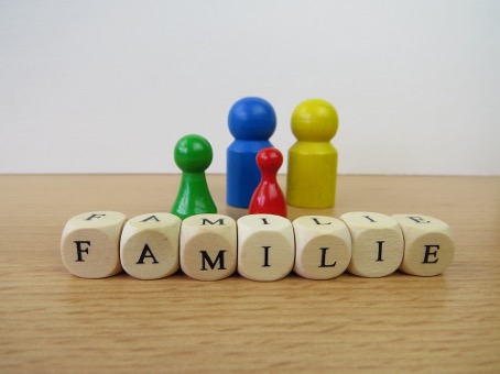 Würfel, die das Wort "Familie" schreiben und im Hintergrund 4 Holz-Spielfiguren