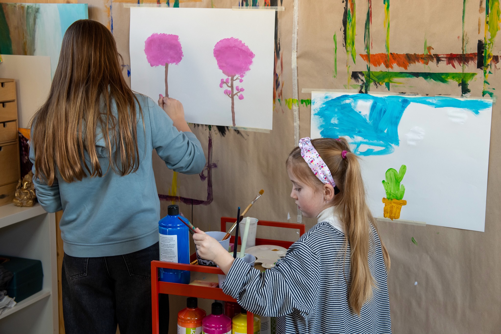 Zwei Kinder bemalen ihre weisse Leinwand an der Wand klebend mit Wasserfarben