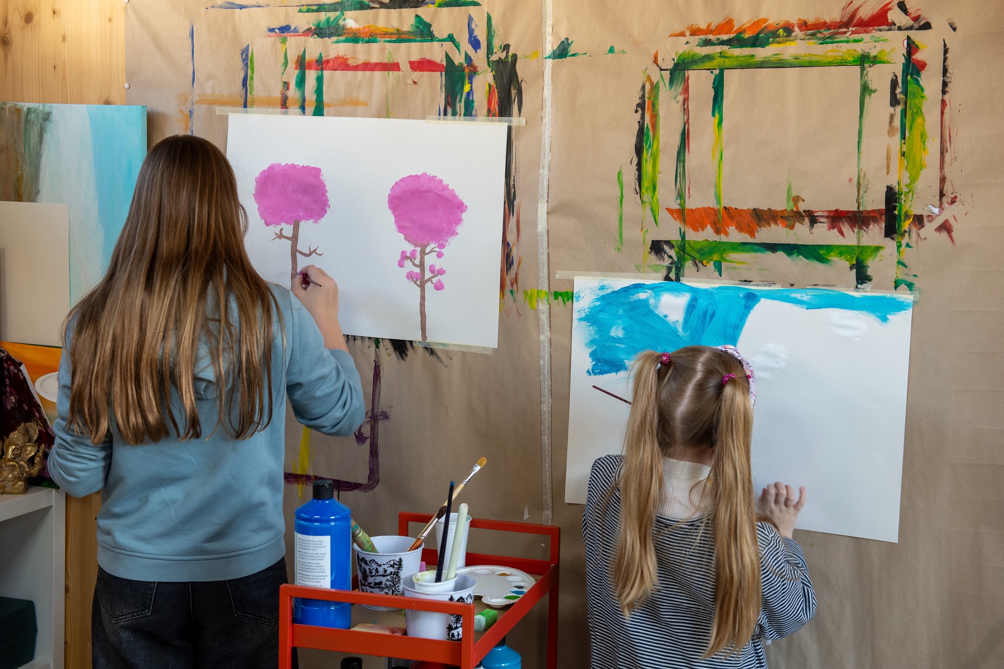Zwei Kinder bemalen ihre weisse Leinwand an der Wand klebend mit Wasserfarben