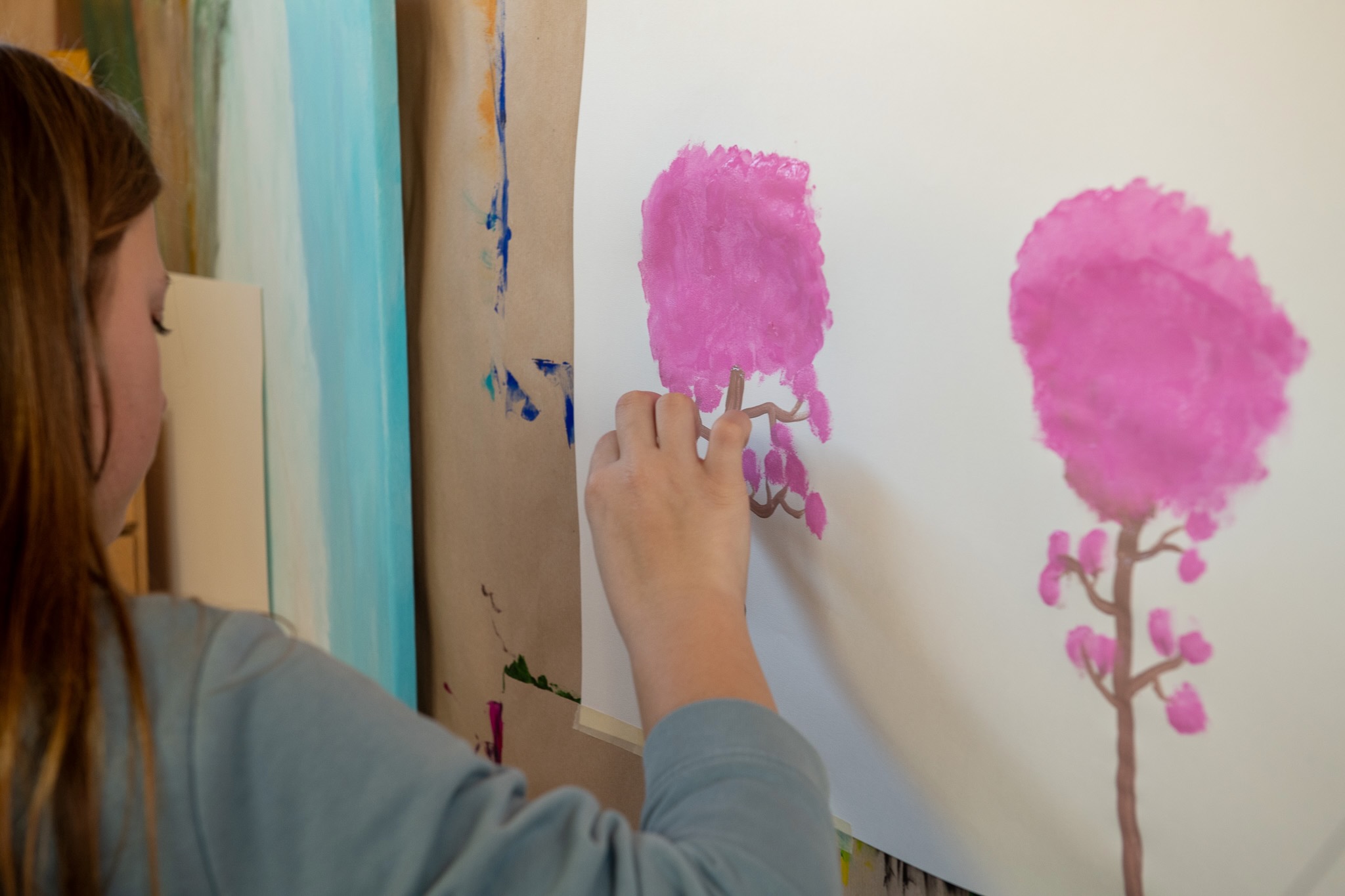 Ein Kind bemalt das weisse Papier an der Wand mit Wasserfarben