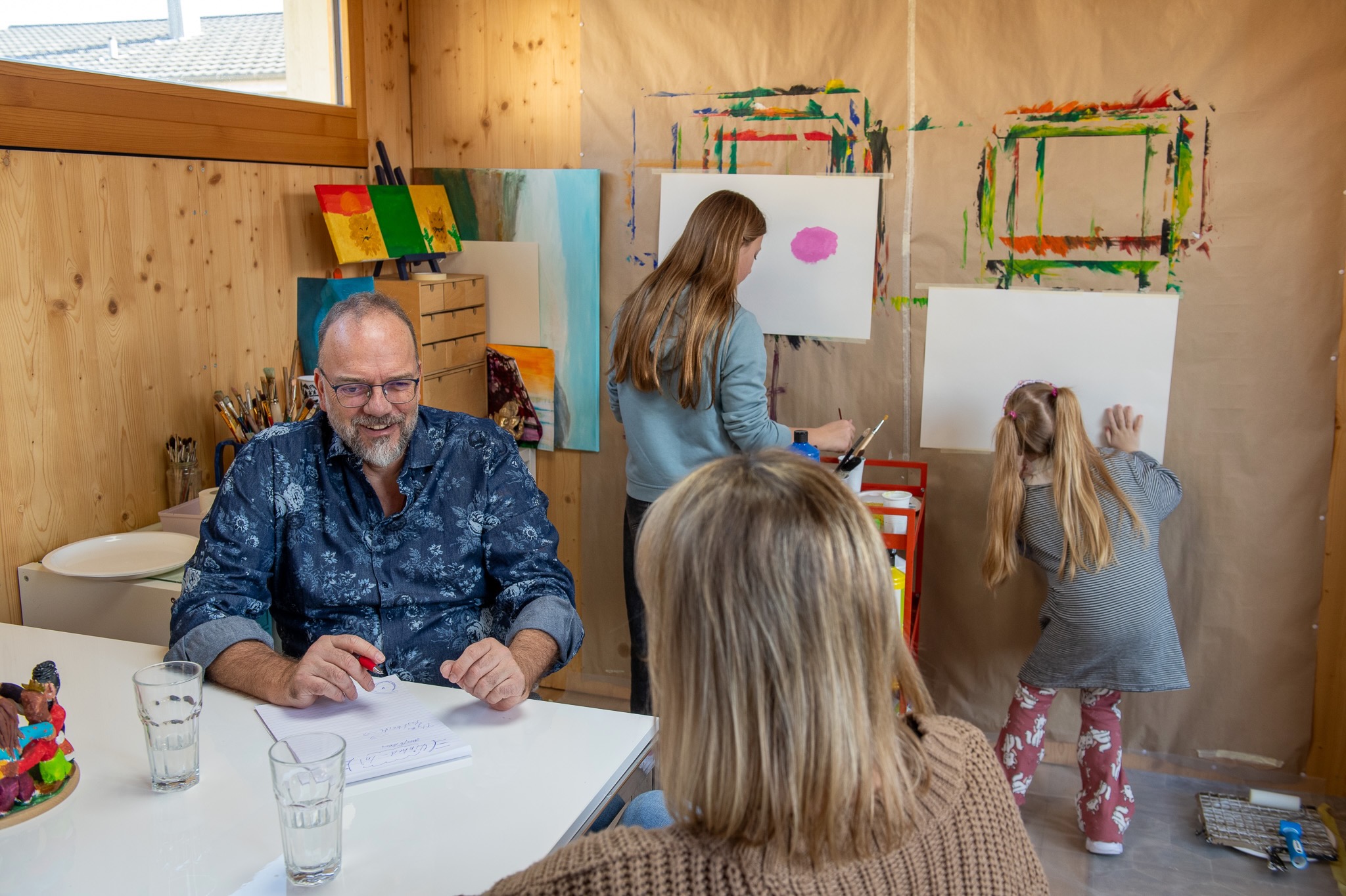 Urs-Michael Hoenner unterhält sich mit einer Mama. Die Kinder malen mit Wasserfarben auf ihr weisses Papier an der Wand.