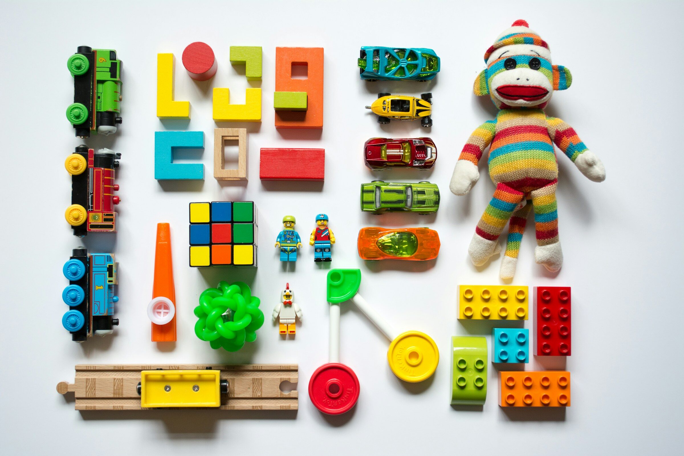 Verschieden farbige Spielzeuge und Puppe systematisch angeordnet und aus der Vogelperspektive fotografiert