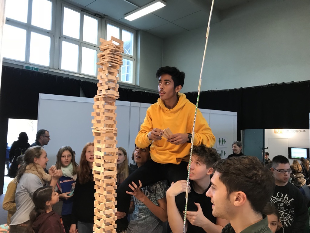 Schüler stehen im Kreis und bauen gemeinsam einen Turm aus Holzklötzchen.